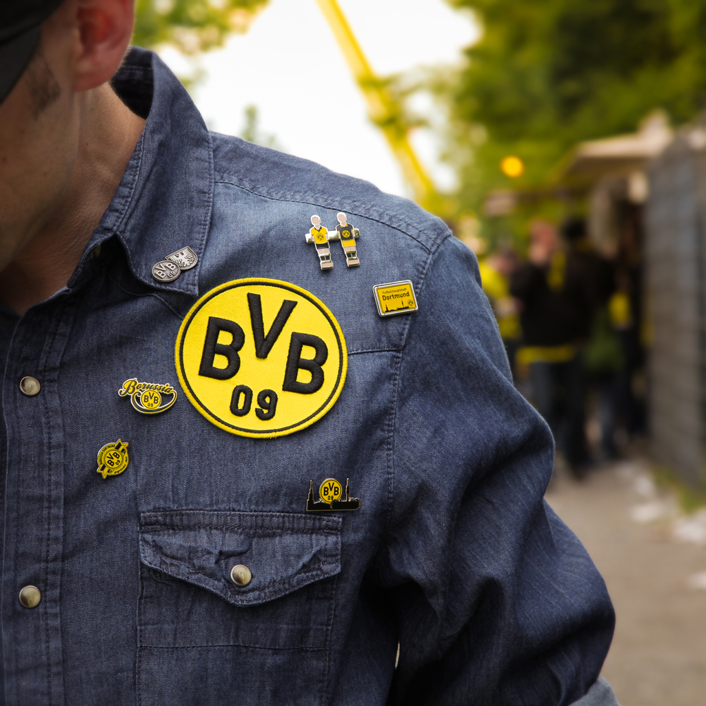 Parche 3D del BVB en negro y amarillo y varios pins del Borussia Dortmund en una chaqueta vaquera, ideal como artículo para aficionados y pieza de colección.