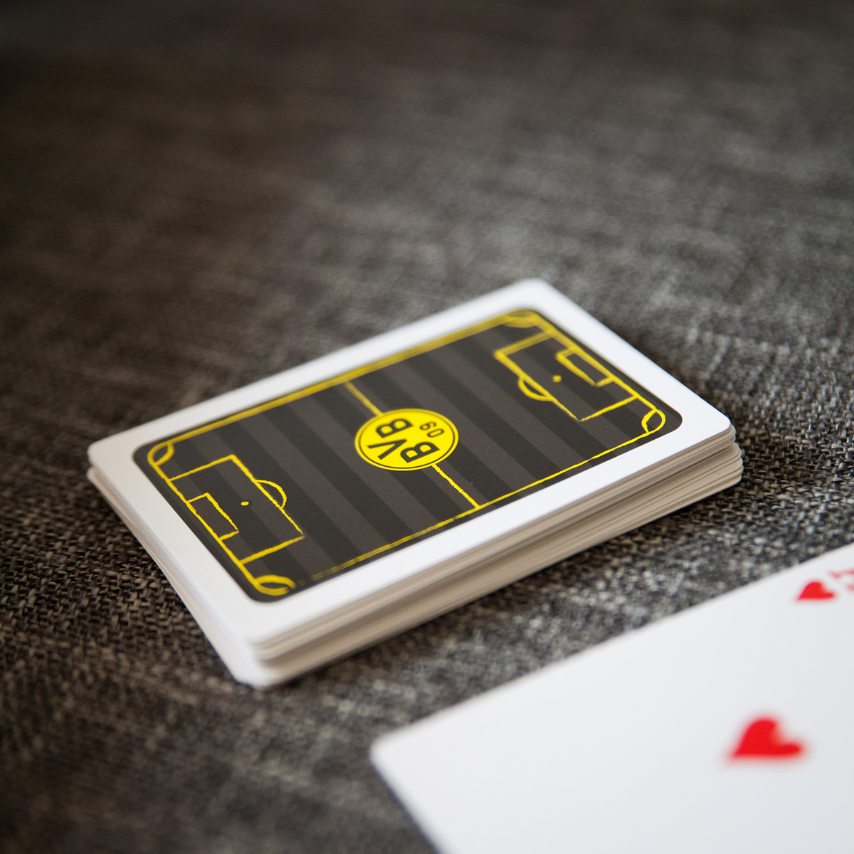 Jeu de cartes de skat du BVB aux couleurs du club, le noir et le jaune, avec un logo BVB bien visible et un motif représentant le terrain au dos des cartes. Un article idéal pour les fans amateurs de skat.