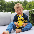 ある子供が、ボルシア・ドルトムントのマスコット「EMMA」の、黒と黄色のチームカラーをあしらった30cmサイズのぬいぐるみを抱きしめ、庭のソファで微笑んでいる。