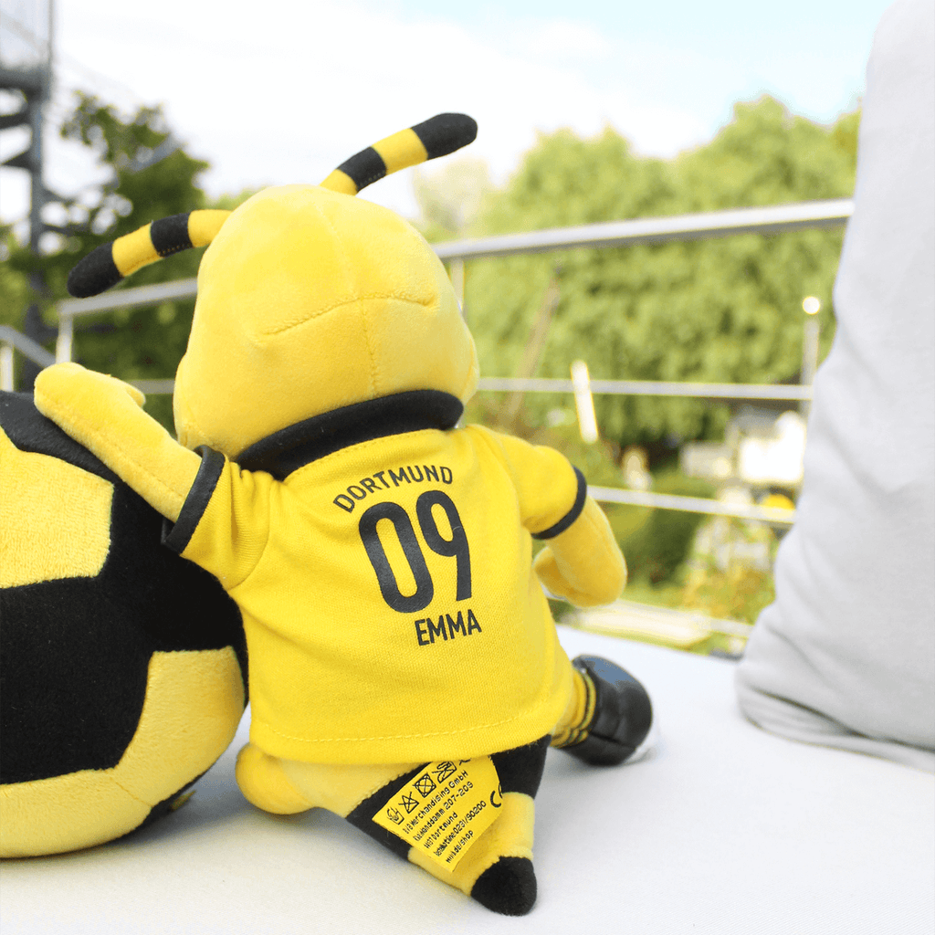 この中型のBVBぬいぐるみは、ボルシア・ドルトムントのマスコット「EMMA」を、'DORTMUND 09'と書かれた黄色のユニフォーム姿で表現しており、その横には黒と黄色のサッカーボールが添えられています。