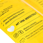 Gros plan sur un emballage jaune comportant un texte imprimé, un symbole en forme de cœur et les mentions « Fabriqué avec amour », ainsi que les icônes des réseaux sociaux de Baeren Company.