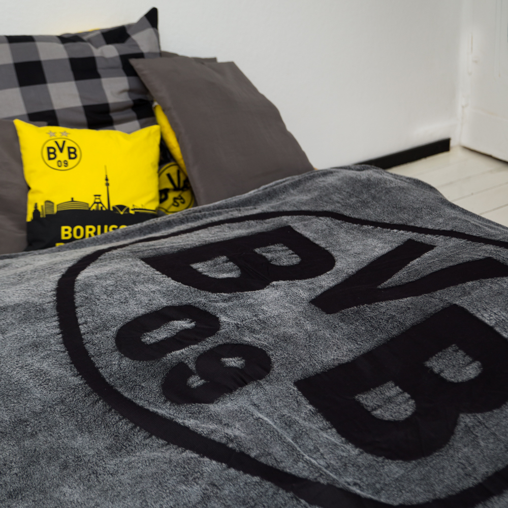 Graue Borussia Dortmund Fleece-Decke aus weichem Material mit großem schwarzen BVB-Logo, ideal für Fans zur Nutzung im Wohnzimmer oder Schlafzimmer.