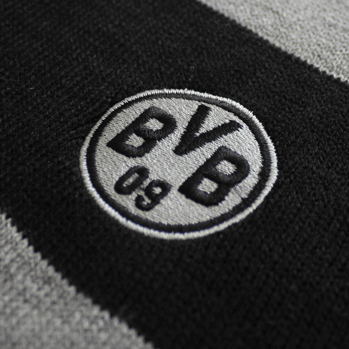 Close-up of a black-and-gray striped BVB scarf with an embroidered Borussia Dortmund logo.