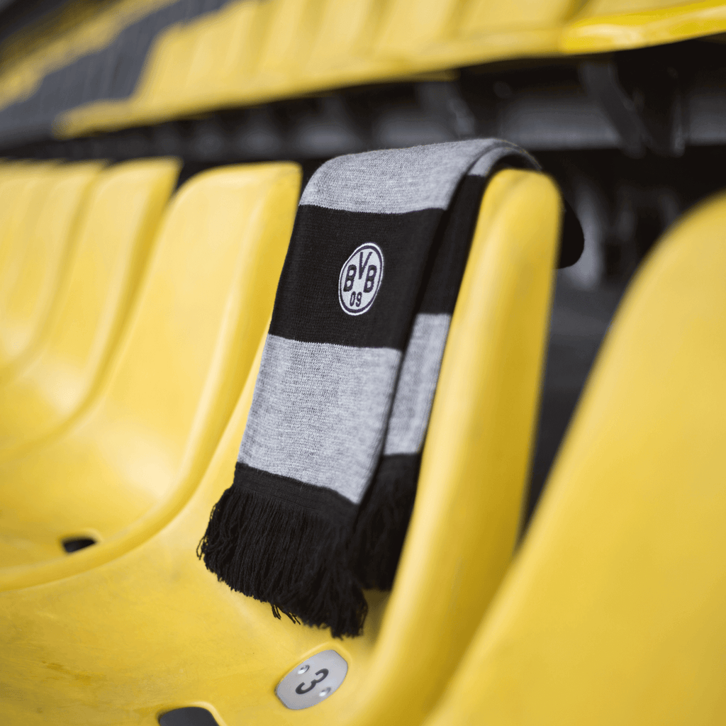 Sciarpa del BVB a righe nere e grigie con frange e logo del BVB ricamato, drappeggiata su un posto a sedere giallo nello stadio.