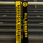 Une écharpe du BVB aux couleurs du club, le noir et le jaune, sur laquelle sont imprimés les slogans « BORUSSIA VERBINDET » et « ALL GENDERS Side by Side », est suspendue à une barre métallique dans l'enceinte du stade.