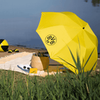 Schwarzgelber BVB-Sonnenschirm mit BVB 09-Logo am Seeufer, umgeben von Strandausrüstung. Perfektes Accessoire für Borussia Dortmund Fans am Strand oder im Freien.