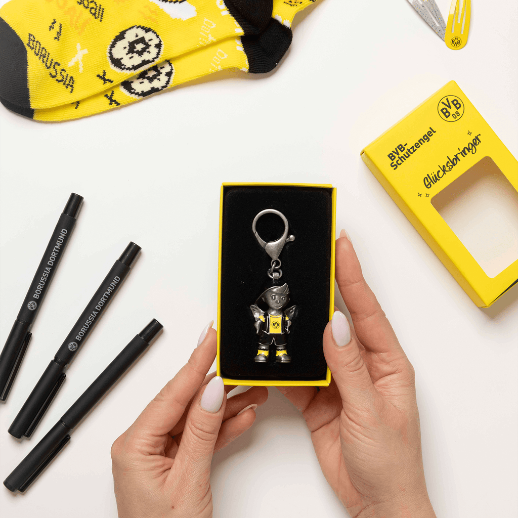 Porte-clés représentant un ange gardien et arborant le logo du BVB, présenté dans un emballage jaune portant l'inscription « Borussia Dortmund » et la mention « porte-bonheur ».
