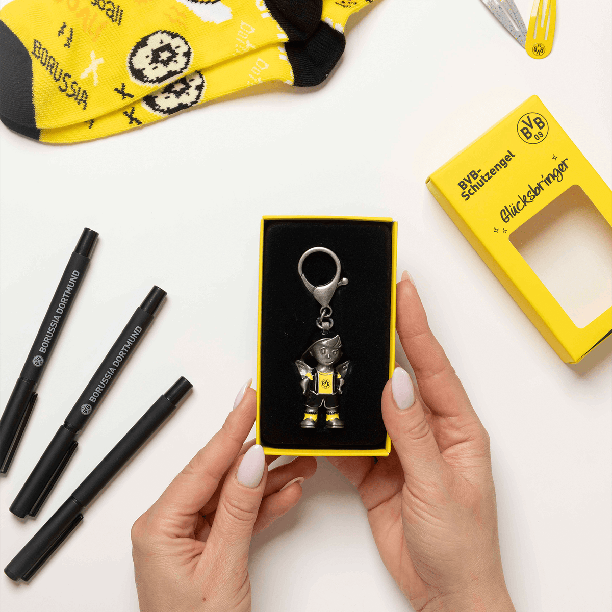 Porte-clés représentant un ange gardien et arborant le logo du BVB, présenté dans un emballage jaune portant l'inscription « Borussia Dortmund » et la mention « porte-bonheur ».