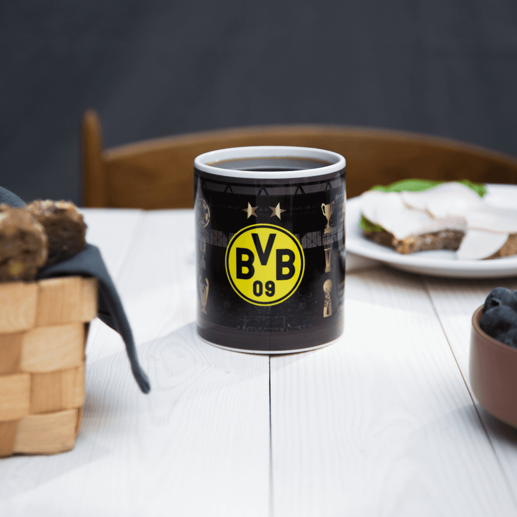 Hochwertige BVB-Tasse mit schwarzgelbem BVB 09-Logo und ikonischen Trophäen auf schwarzem Hintergrund. Ideal für Fans von Borussia Dortmund.