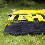 Black-and-yellow BVB beach towel with emblem, measuring 100x150 cm, shown on a meadow. Perfect for Borussia Dortmund fans.