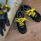 Black-and-yellow Atlas BVB S3 Malocher 09 safety shoe, placed on a wooden floor with work gloves and tools in the background.