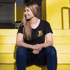 Camiseta negra del BVB para mujer de la colección para socios, con el logotipo amarillo y la inscripción «Borussia Dortmund», que luce una joven en unas escaleras amarillas.