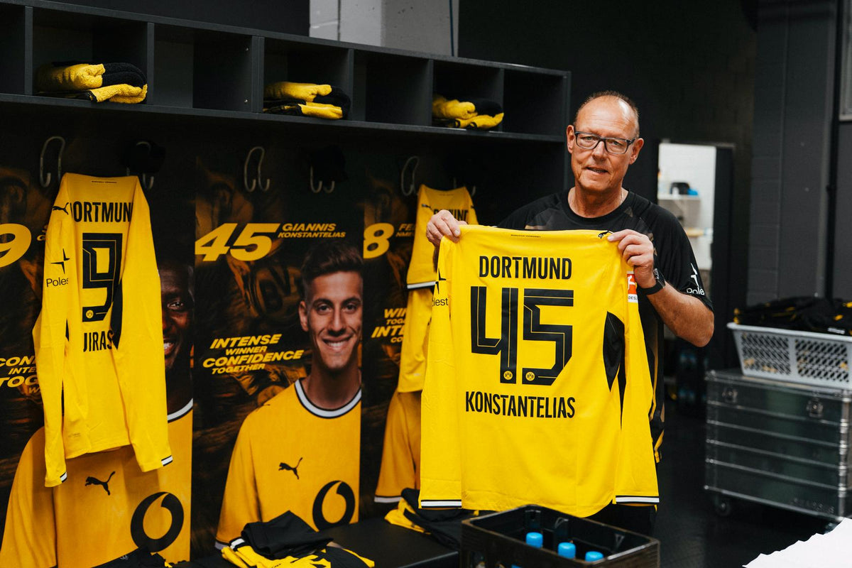 Frank Gräfen, der Zeugwart von Borussia Dortmund steht in der Mannschaftskabine des BVB im SIGNAL-IDUNA-PARK und hält lächelnd das Authentic Trikot des Spielers Konstantelias mit der Nummer 45 in die Kamera.