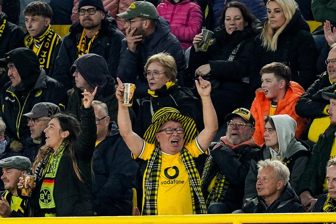 Zu sehen ist die Fantribüne hinter der Spielerbank bei einem BVB Heimspiel im SIGNAL-IDUNA-PARK. Die Tribüne ist gefüllt mit Fans, im Mittepunkt steht der bekannte Fan Gerd, der in Hut, Schal und Authentic Trikot am mitfiebern ist.