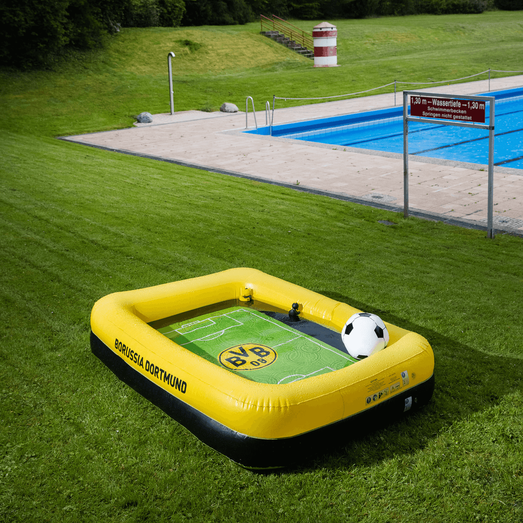 Aufblasbarer BVB-Pool in schwarzgelber Optik mit Fußball-Design, aufgestellt auf einer grünen Wiese neben einem Freibad.