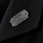 Silberfarbener Borussia-Dortmund-Pin mit Rote-Erde-Stadionumrissen und BVB-Logo, präsentiert in einer Detailaufnahme auf schwarzem Stoff.