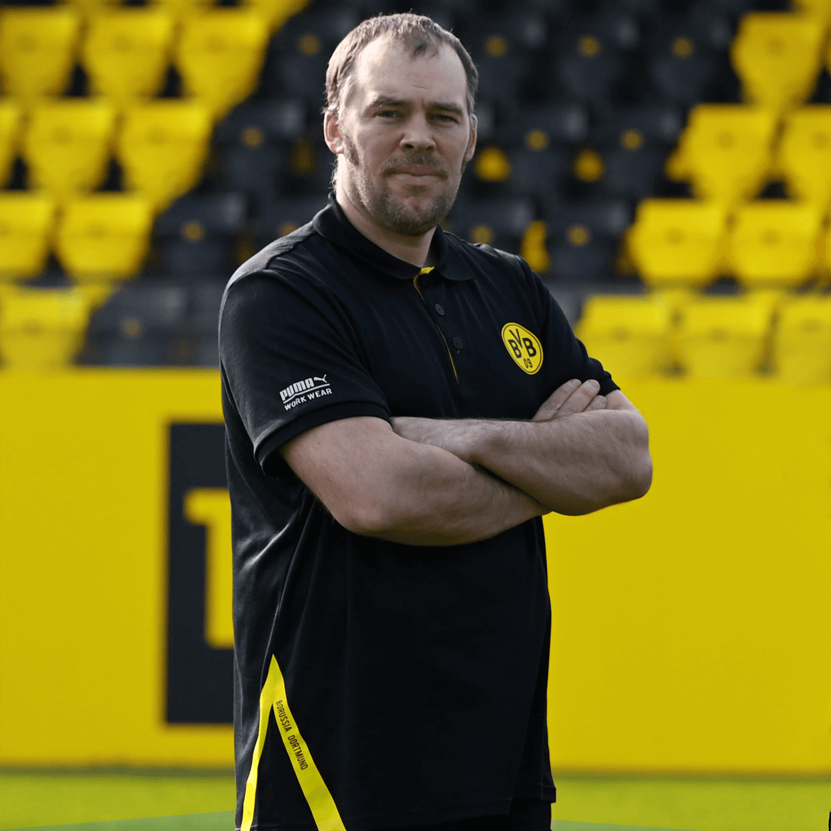 Schwarzes Borussia Dortmund Arbeitspolo für Herren mit gelbem BVB-Logo auf der Brust und PUMA-Branding, aufgenommen im SIGNAL IDUNA PARK.