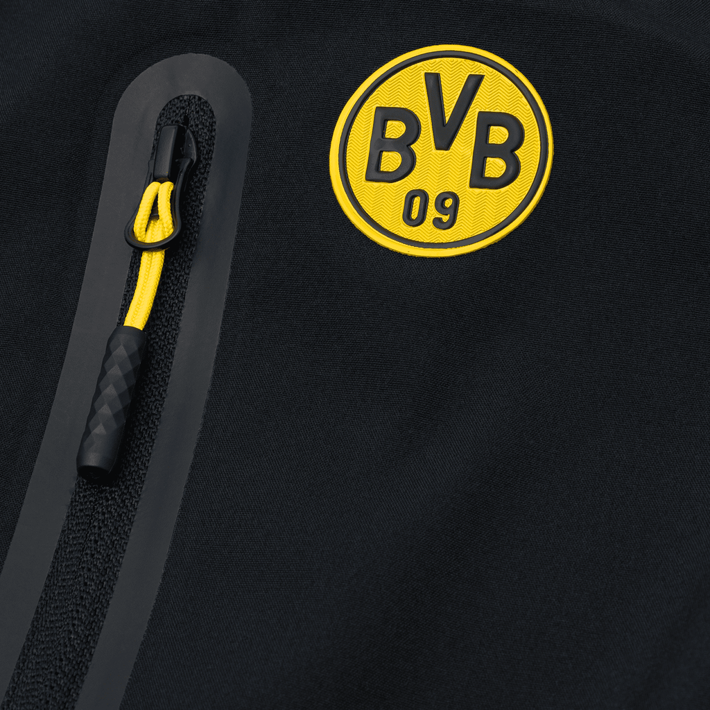 Detailaufnahme einer schwarzgelben BVB-Softshelljacke für Kinder, mit prominentem BVB-Emblem und gelber Zipper-Schlaufe.