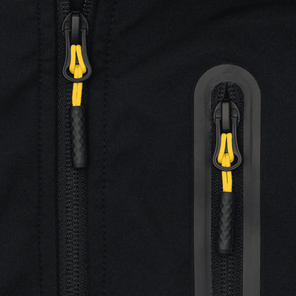 Primer plano de un detalle de la cremallera negra y amarilla de la chaqueta softshell del BVB para mujer, un artículo oficial para aficionados con un diseño elegante.