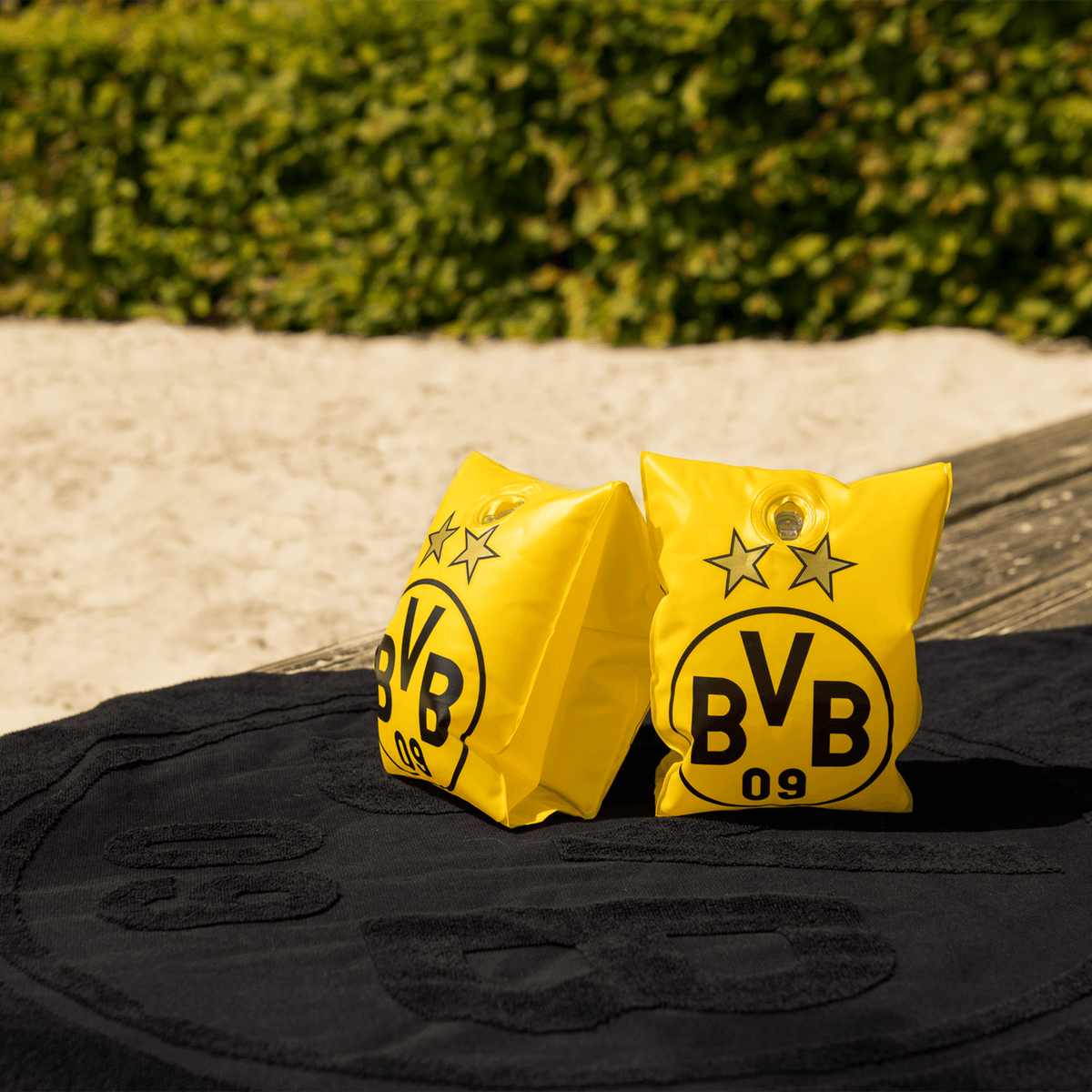 BVB swim wings in black and yellow with the BVB logo and two stars, ideal for children ages 1 to 6, shown on a beach with a towel in the background.