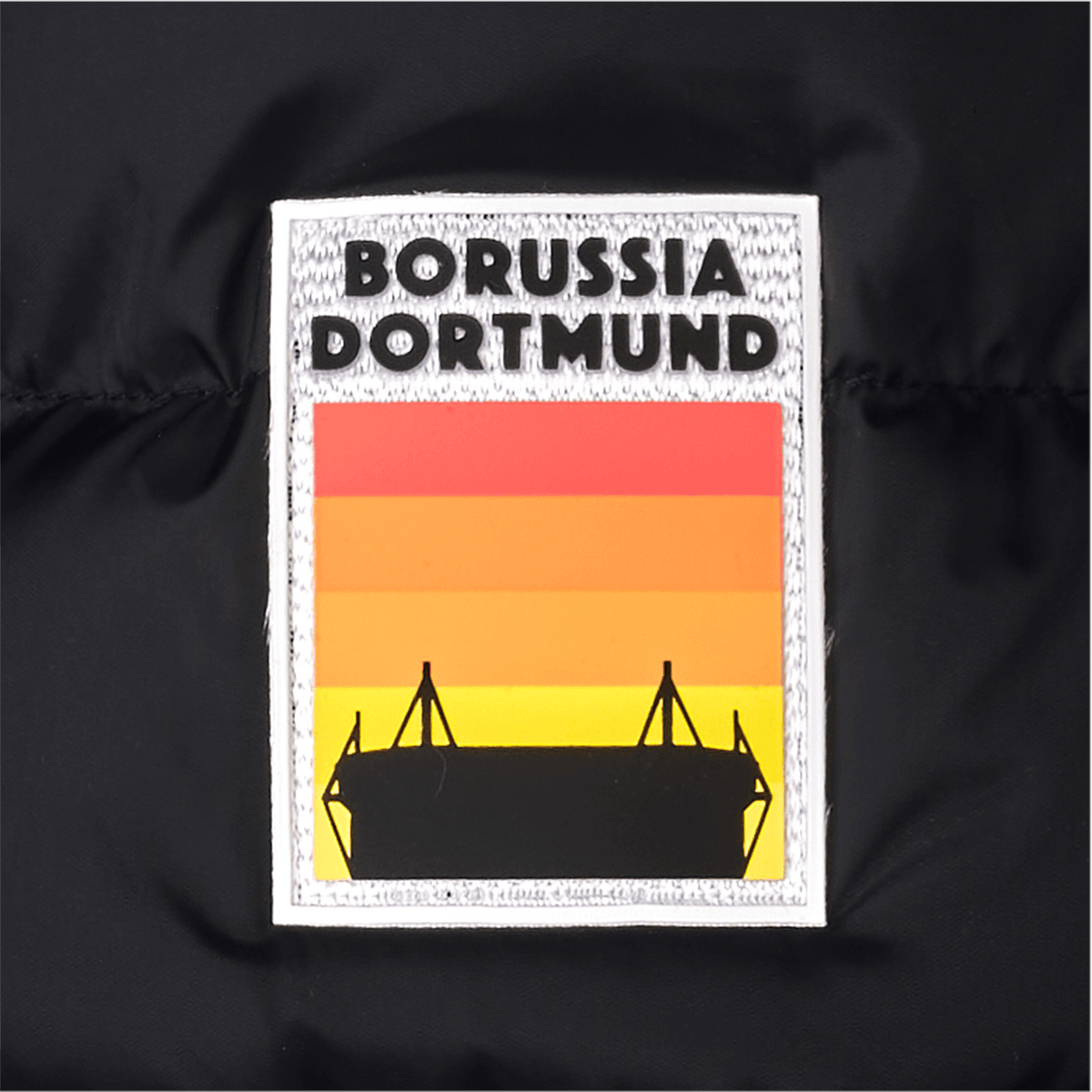 Steppjacke für Damen in Schwarz mit einem stilisierten Stadion-Patch in schwarzgelb, Rot-Orange-Tönen und dem Schriftzug Borussia Dortmund auf der Brust.