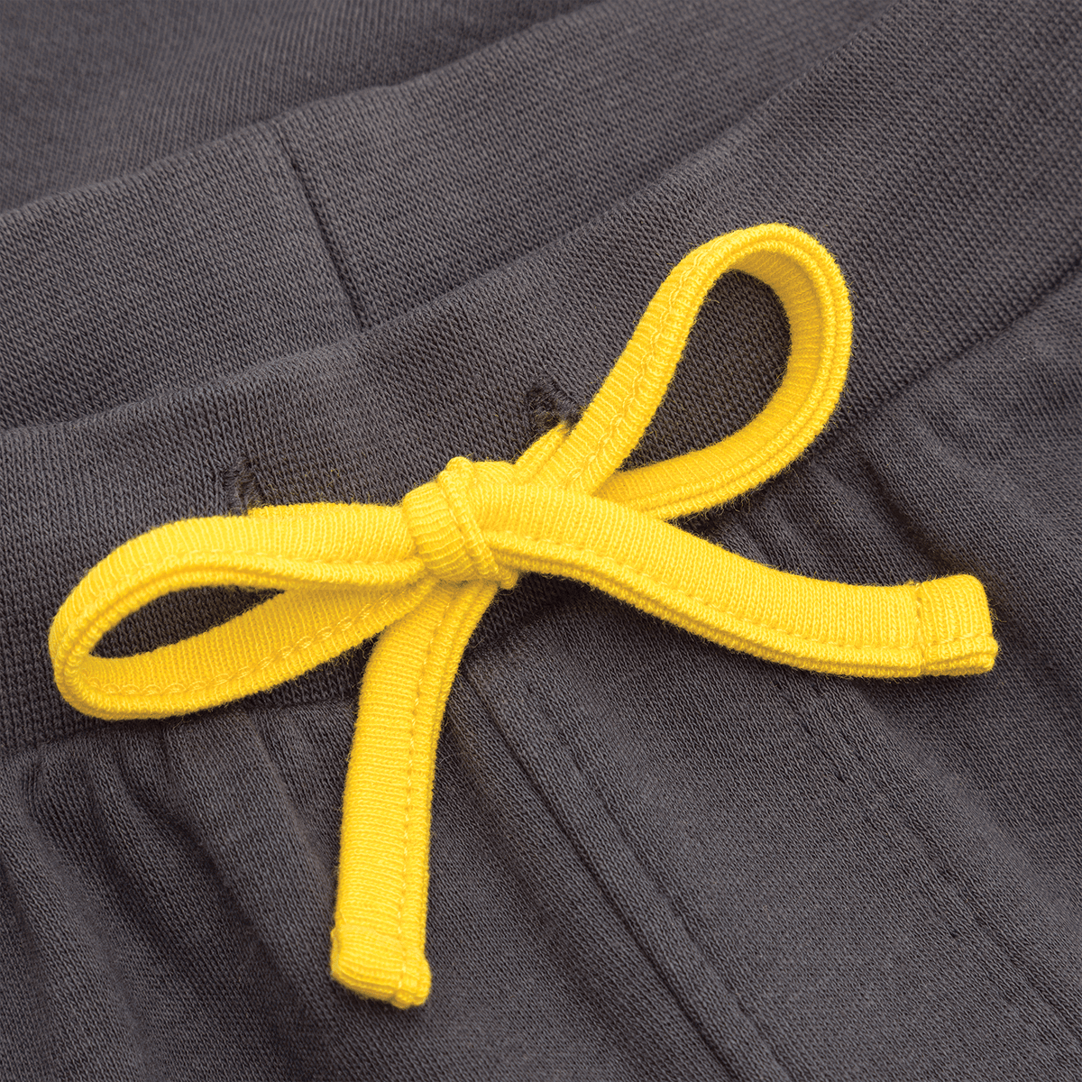 Detailaufnahme einer BVB-Kinderhose in schwarz mit auffälliger gelber Zierschleife aus einer Kordel, ideal für junge Fans von Borussia Dortmund.