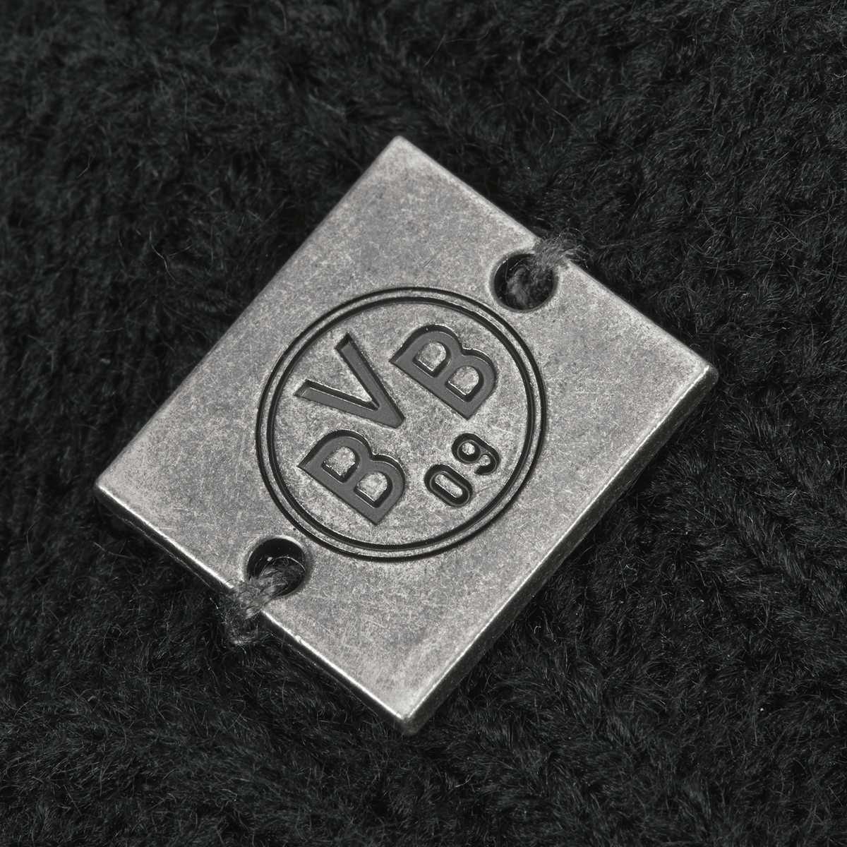 Detailaufnahme einer BVB 09 Bommelmütze für Damen in Schwarz mit einem Metall-Logo und eingeprägtem BVB 09 Schriftzug.