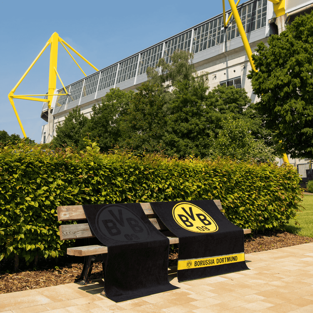 Serviette de bain noire du BVB, ornée d'un grand logo du BVB et de l'inscription « Borussia Dortmund », posée sur un banc en bois devant le SIGNAL IDUNA PARK.