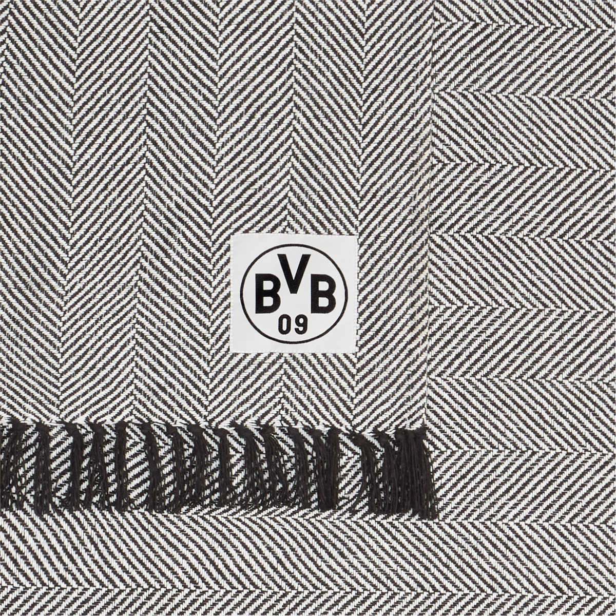 Couverture en coton noir et blanc du Borussia Dortmund, motif en chevrons, dimensions 150 x 200 cm, avec le logo du BVB et des franges noires, certifiée GOTS.