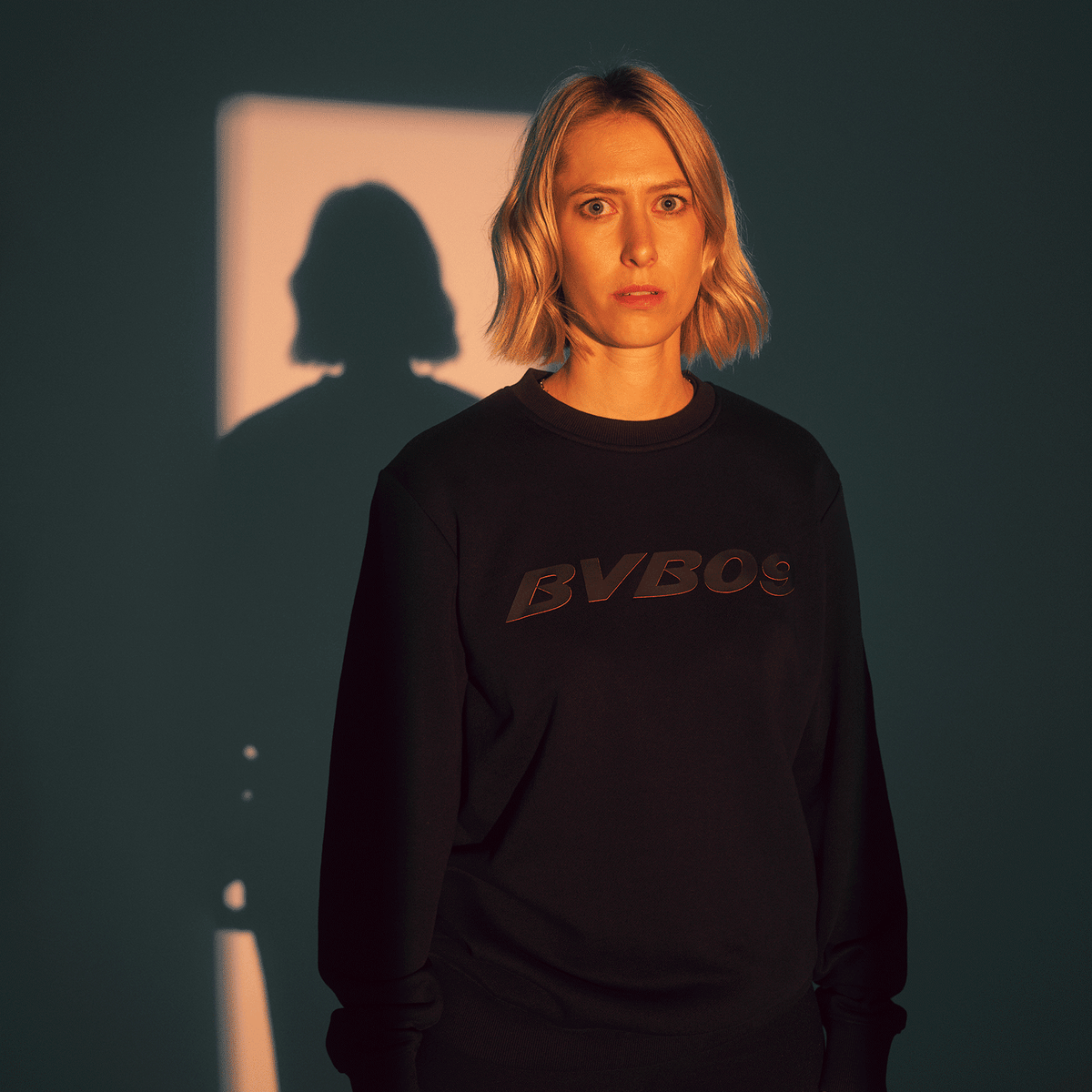 A black BVB sweater with "BVB 09" lettering in an elegant design, shown from the front, worn by a woman under atmospheric lighting.