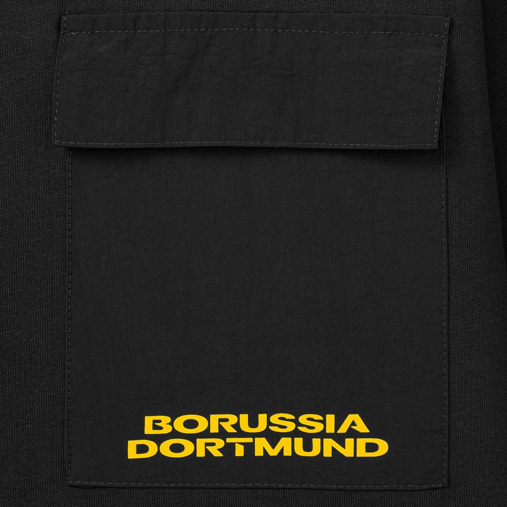 Camiseta negra del BVB con bolsillo en el pecho y el nombre «Borussia Dortmund» en amarillo, artículo para aficionados del equipo de fútbol.