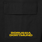 Primo piano di una giacca nera a girocollo con tasca applicata e logo giallo del Borussia Dortmund.