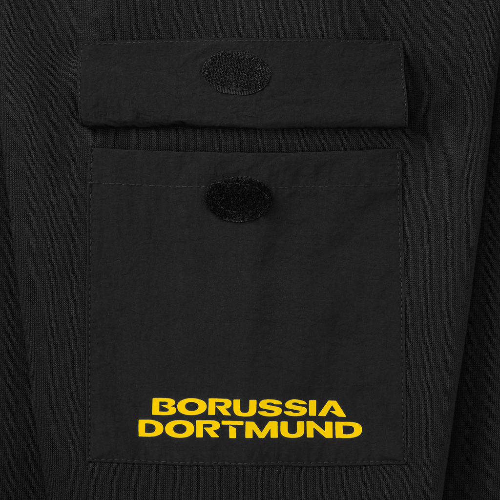 Gros plan sur une poche poitrine du pull à col rond noir du BVB, orné du logo jaune du Borussia Dortmund, idéal pour les supporters du club.