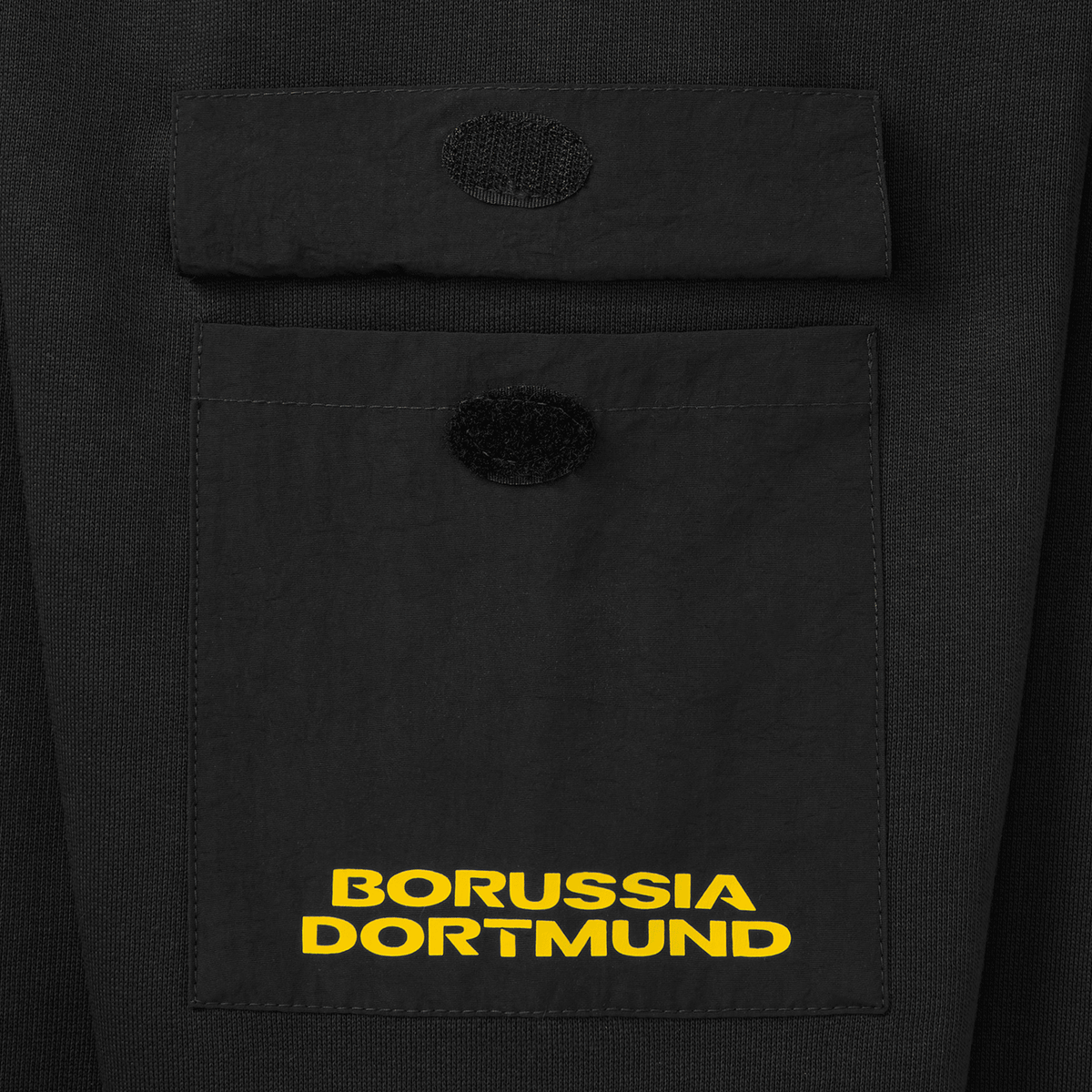 Gros plan sur une poche poitrine du pull à col rond noir du BVB, orné du logo jaune du Borussia Dortmund, idéal pour les supporters du club.