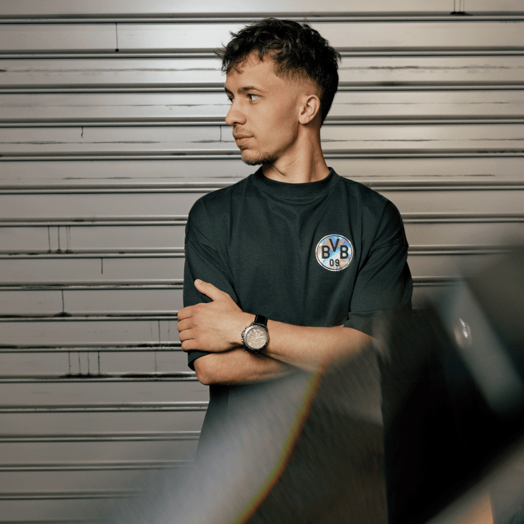 T-shirt noir « BVB Rainbow » avec le logo rond « BVB 09 » sur la poitrine gauche, porté par un homme devant un mur métallique.