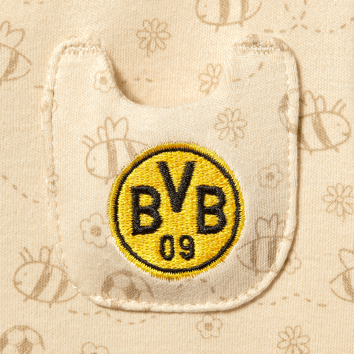 Detailaufnahme des BVB Babyschlafanzugs mit gesticktem BVB 09 Logo und Bienenmuster auf beigem Stoff, ideal für kleine BVB-Fans.
