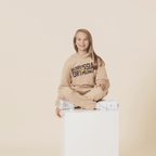 Pantaloni della tuta beige del BVB per bambini, abbinati a una felpa con cappuccio coordinata, presentati da un bambino sorridente su un piedistallo bianco.