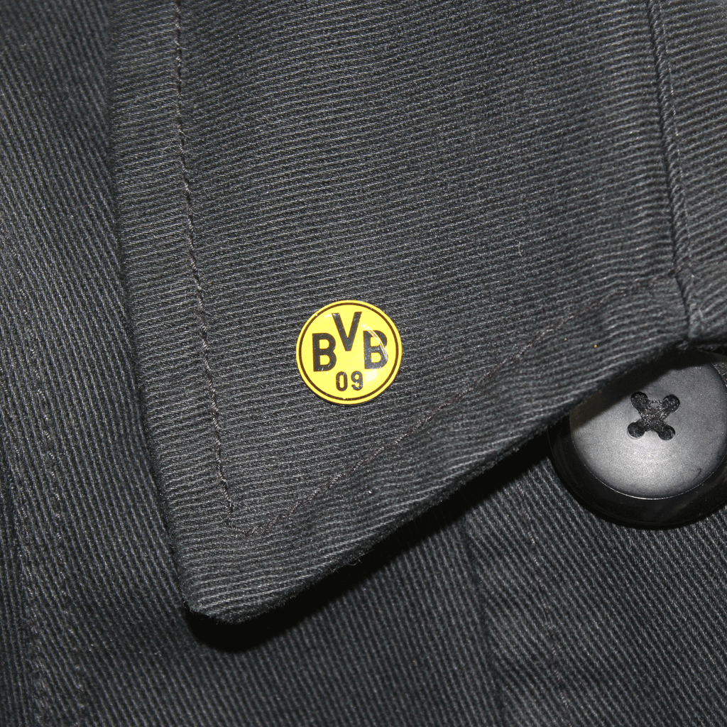 エンブレムと「BVB 09」の文字が入った黄色いBVBピン。黒い布の上に写っています。ボルシア・ドルトムントのファンにぴったりです。