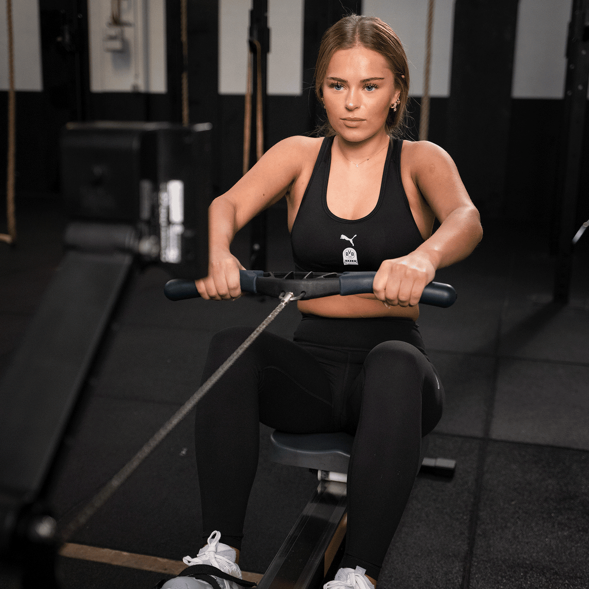 Collant noir BVB x Puma Gym Cloudspun pour femme, porté par une femme qui s'entraîne sur un rameur en salle de sport.
