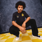 The BVB KidSuper Graphic T-shirt for adults in black with yellow accents, the BVB emblem, and the PUMA logo on the chest. Ideal for Borussia Dortmund fans.