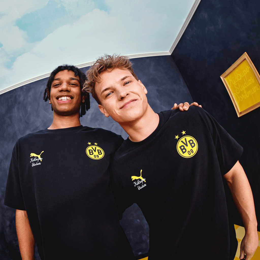 BVB KidSuper Graphic T-shirt in black with a yellow BVB logo and Puma emblem, worn by two men against a stylish background.