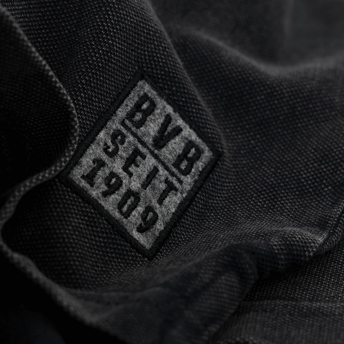 Schwarzer Stoff mit aufgenähtem BVB-Logo und Schriftzug 'BVB seit 1909' in Grau, Detailaufnahme von Fanartikel-Textil.