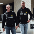 Zwei Männer präsentieren einen schwarzen BVB-Hoodie und eine schwarze BVB-Jacke mit gelbem Borussia Dortmund-Logo und Schriftzug, ideal für Freizeit und Fanmode.