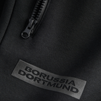 Pantalones de chándal negros «BVB Essentials» con el logotipo del Borussia Dortmund y cremallera, mostrados en detalle.