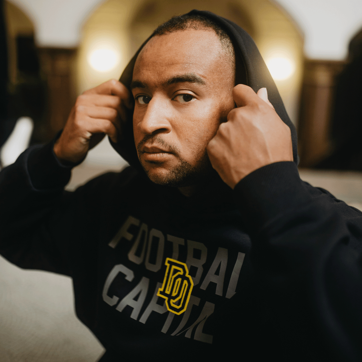 Sudadera con capucha negra del BVB College con el logotipo amarillo y la inscripción «Football Capital», ideal para los aficionados del Borussia Dortmund.