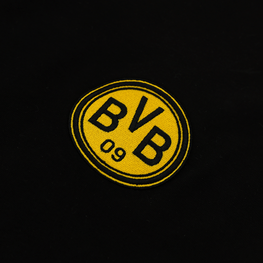 T-shirt noir « Iconic Lifestyle » du BVB, orné d'un emblème jaune bien visible « BVB 09 ». Gros plan sur le logo à l'avant du t-shirt.