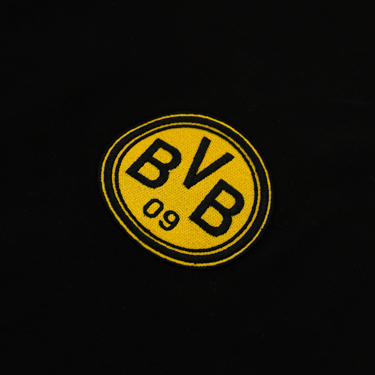 T-shirt noir « Iconic Lifestyle » du BVB, orné d'un emblème jaune bien visible « BVB 09 ». Gros plan sur le logo à l'avant du t-shirt.