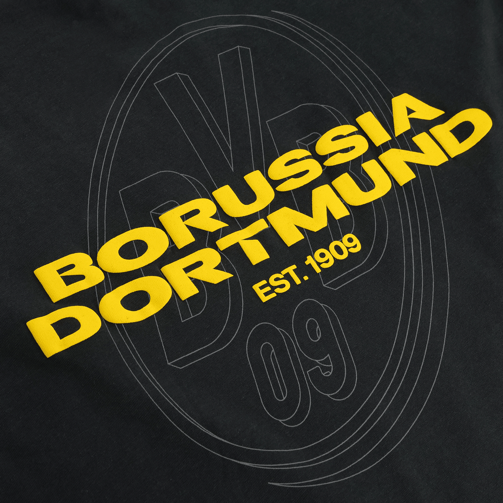 黄色いボルシア・ドルトムントのロゴと「EST. 1909」の文字が入った、黒のBVB Urban Tシャツのクローズアップ写真。ファンに最適です。