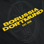 Primo piano di una maglietta nera BVB Urban con il logo giallo del Borussia Dortmund e la scritta “EST. 1909”; ideale per i tifosi.