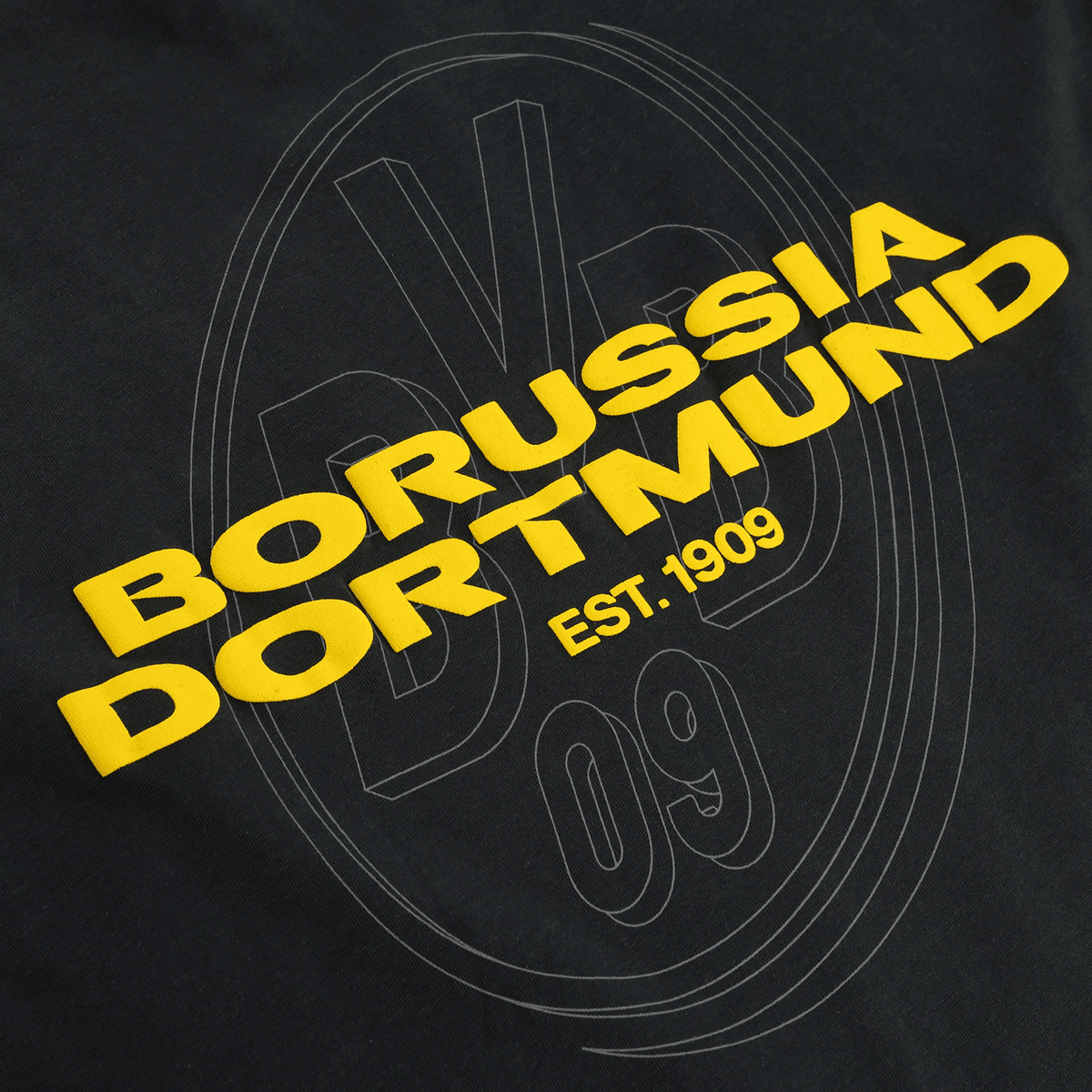 Primo piano di una maglietta nera BVB Urban con il logo giallo del Borussia Dortmund e la scritta “EST. 1909”; ideale per i tifosi.